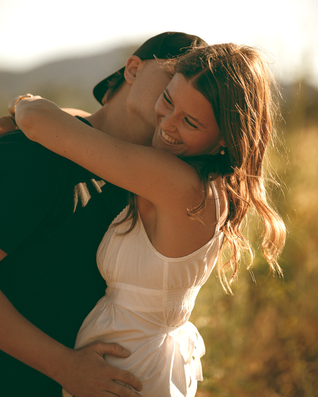 Couple embracing and laughing in a golden sunlit field at sunset